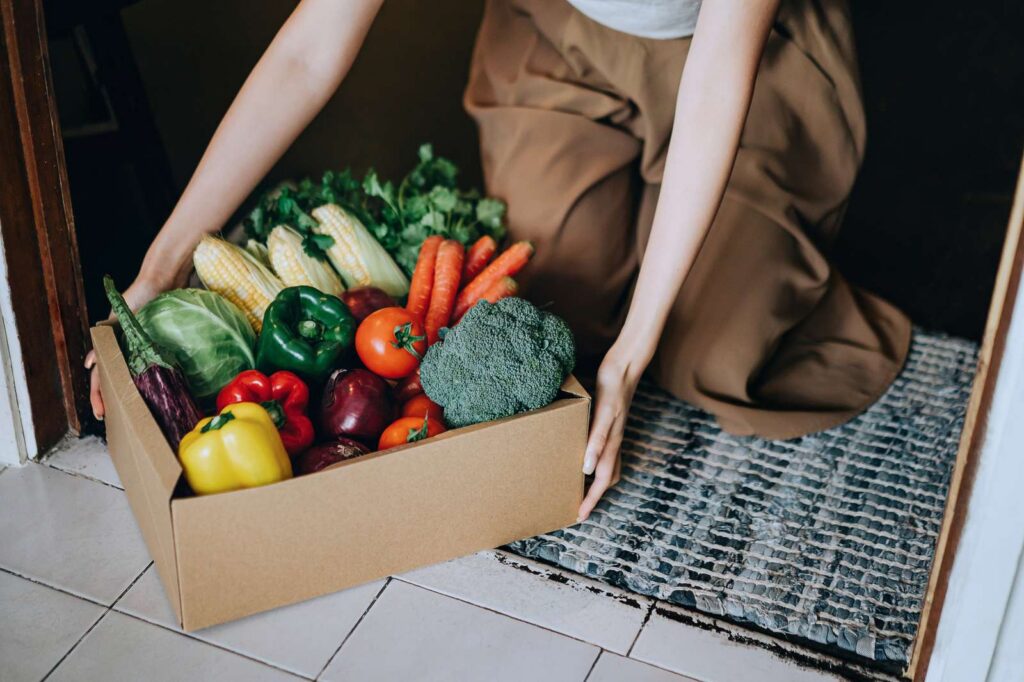 A woman receiving a box of fresh organic produce at her front door.